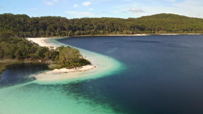 A stunning, static aerial view captures a beautiful freshwater lake with a white sand spit separating shallow turquoise water from the deep blue