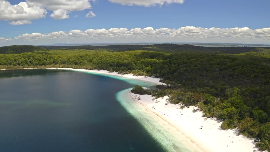 An incredible aerial view slowly reveals a pristine lake with stunningly white sand beaches, encircled by a dense green forest