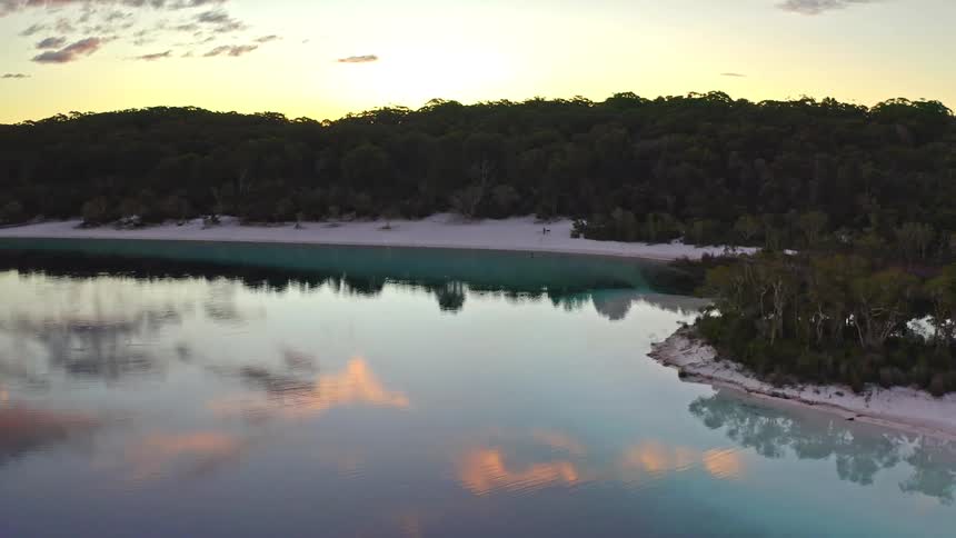 An awe-inspiring aerial view captures a pristine freshwater lake with white sand beaches, beautifully reflecting the vibrant colors of the sunset