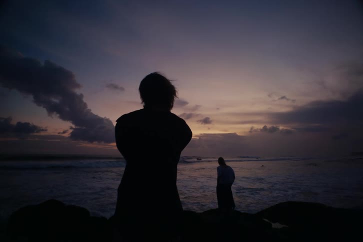 Silhouettes of two people on a rocky beach watching the ocean waves roll in at sunset