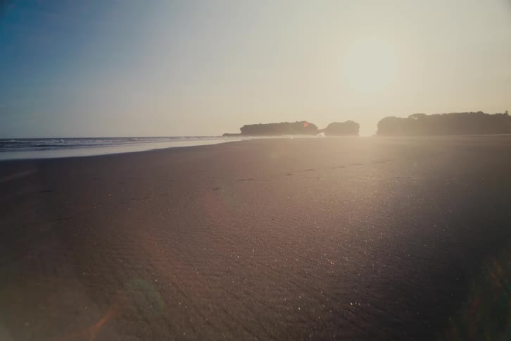 A tranquil, low-angle shot of a sandy beach at sunrise with the ocean and a hazy coastline in the distance