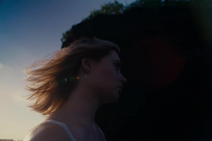 Slow motion close-up of a thoughtful woman with her hair blowing in the wind as she looks towards the golden sunset sky