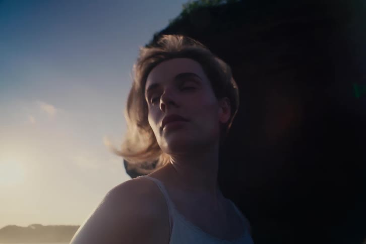 Introspective close-up of a beautiful young woman bathed in the warm light of sunset with her hair blowing in the wind