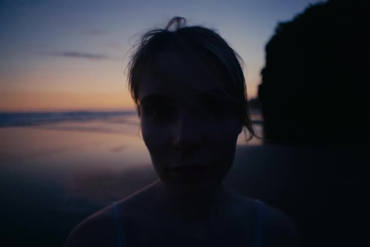 An intimate close-up portrait of a young woman's face in silhouette against a beautiful sunset on the beach