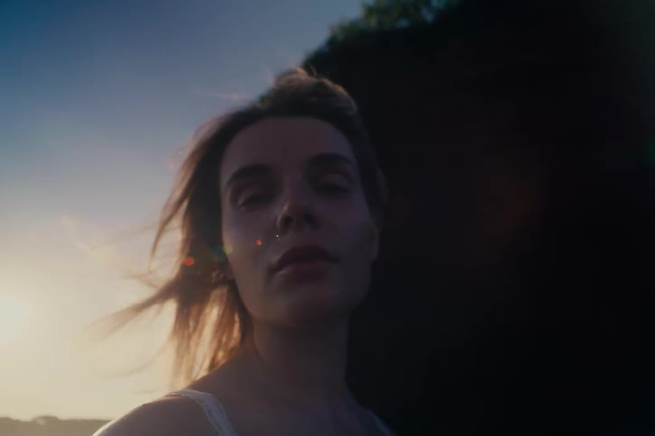 A contemplative young woman's face is illuminated by the warm sunset light as her hair blows in the breeze