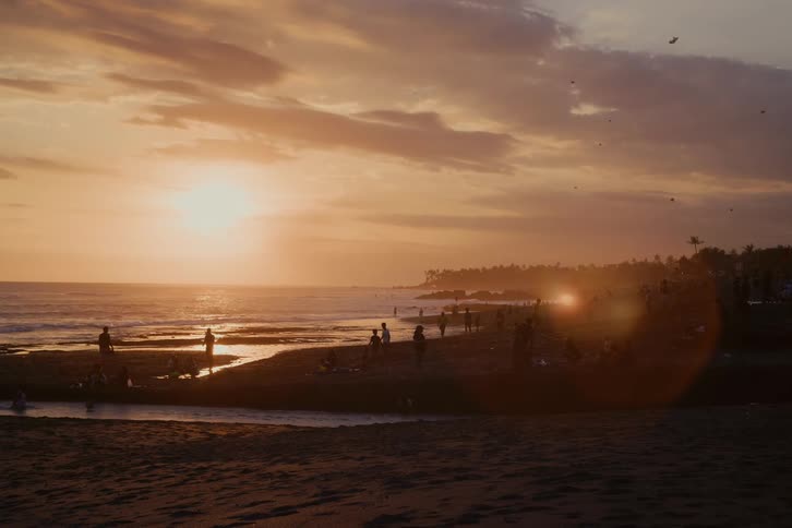 Silhouettes of people enjoying a beautiful golden sunset on a bustling tropical beach