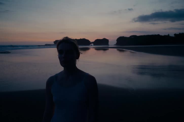 Portrait of a silhouetted young woman looking out at the ocean on a moody beach at dusk