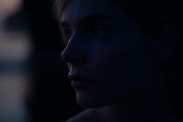 Close-up profile of a serious young woman's face cast in deep shadows at night