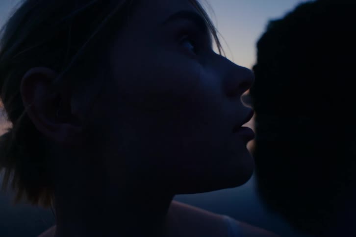 Close up of a pensive young woman's face silhouetted against the serene twilight sky over a calm body of water