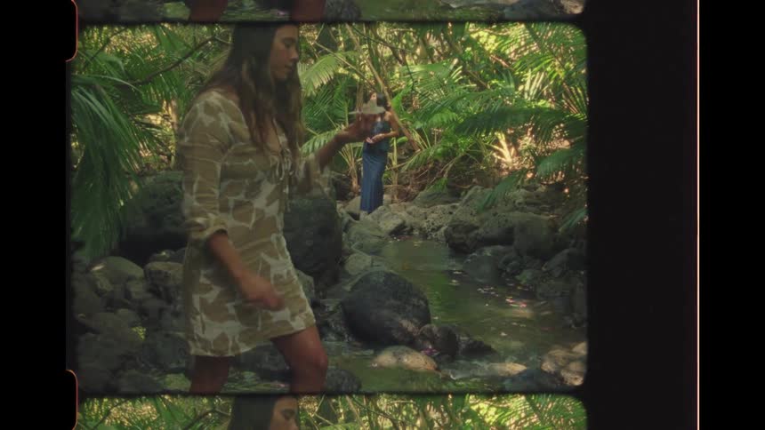 A woman collects a flower from a stream deep in a lush jungle, as another watches on in this vintage-style footage