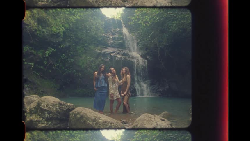 Three young women pose together in the water at the base of a beautiful jungle waterfall in this vintage-style footage