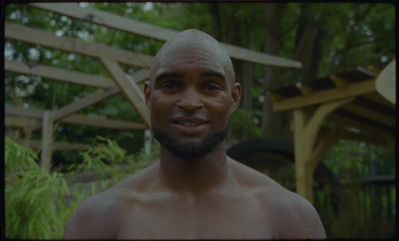 A vintage-style portrait of a smiling shirtless man outdoors in a lush green environment