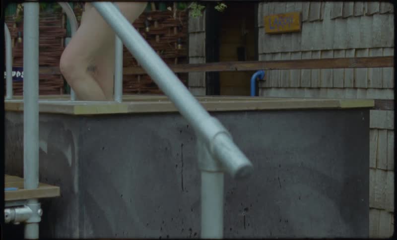 A woman with red hair and tattoos enters a steamy outdoor hot tub in this grainy, vintage-style footage