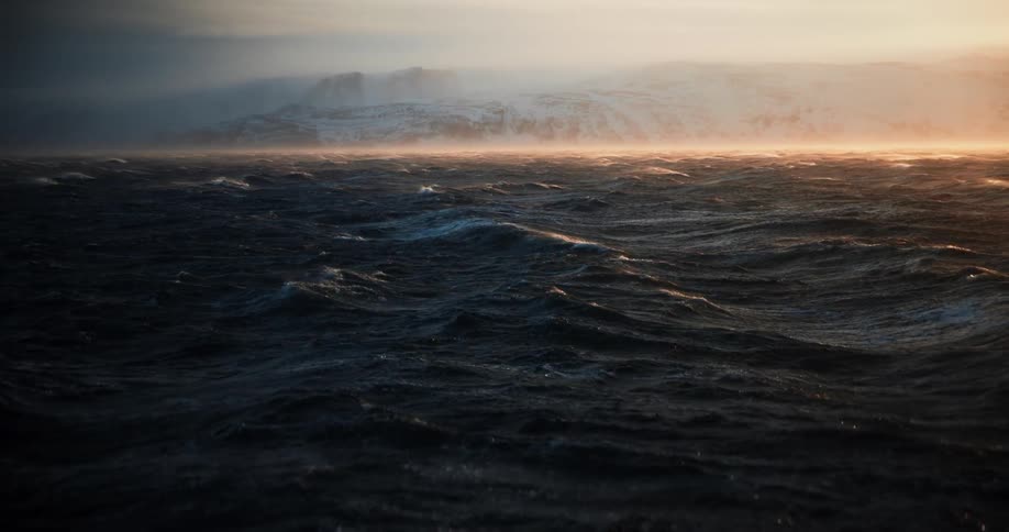 Dramatic slow motion footage captures the churning, dark sea during a fierce winter storm at sunrise with a snow-covered coastline in the distance