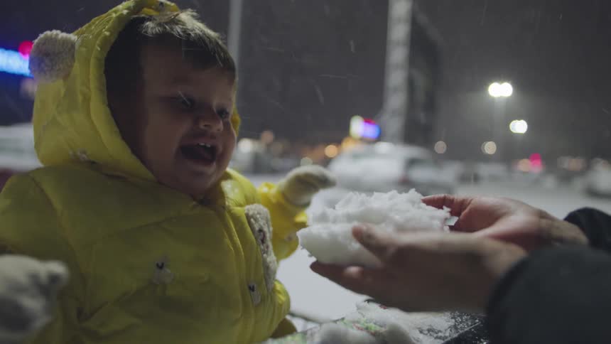 An adorable baby in a yellow snowsuit experiences snow for the first time, laughing with joy before looking on with wonder