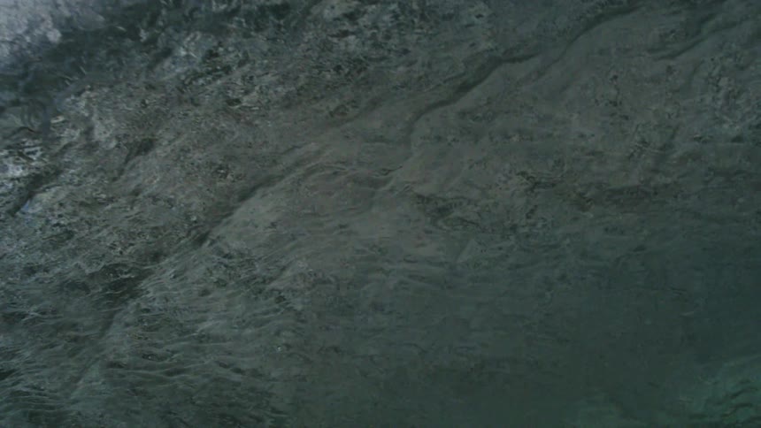 A dramatic slow-motion underwater perspective captures a powerful ocean wave as it crests, breaks, and churns overhead