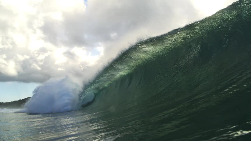 A massive, backlit ocean wave forms a perfect barrel as it crashes towards the camera in dramatic slow motion