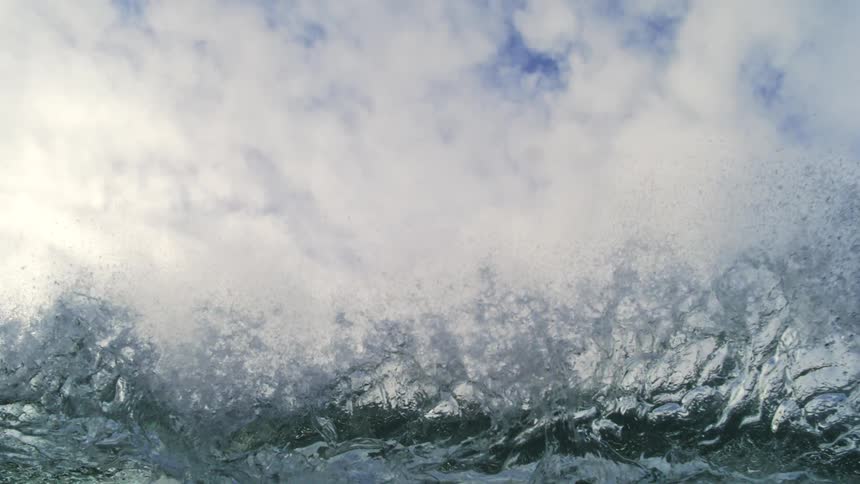 A dramatic super slow-motion shot captures a massive, dark wave cresting against a cloudy sky before it breaks and engulfs the camera