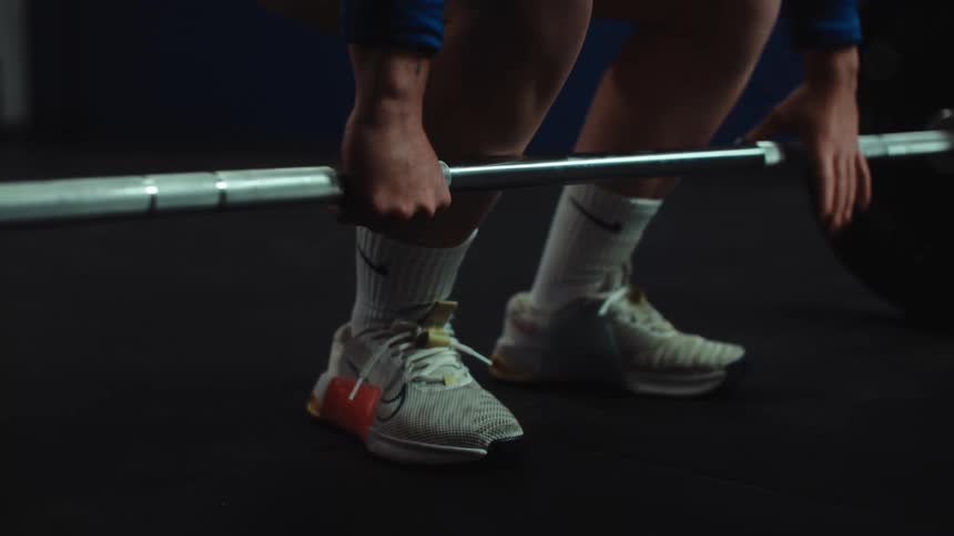 Close up shot of an athlete's hands gripping a heavy barbell as they prepare for a deadlift in a dark gym