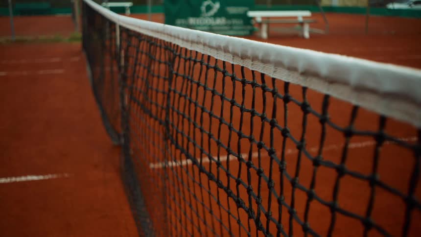 A tennis ball hits the net on a red clay court in a slow-motion close-up