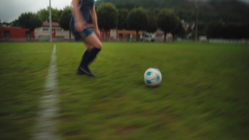Dynamic low-angle shot of a soccer player dribbling the ball down the field and kicking it