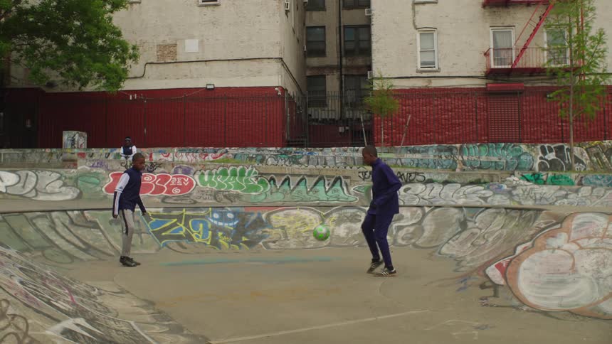 Slow motion shot of two young boys casually playing soccer in a graffiti-covered skatepark