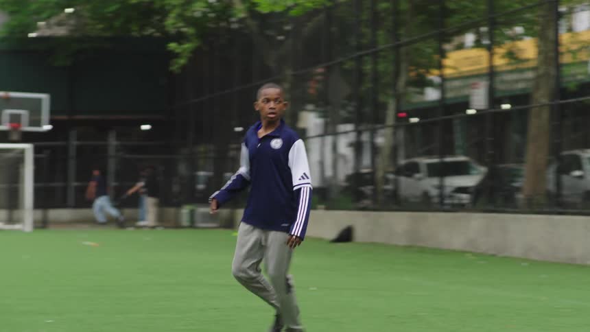 A young boy dribbles a soccer ball on a city field and kicks it with power in slow motion