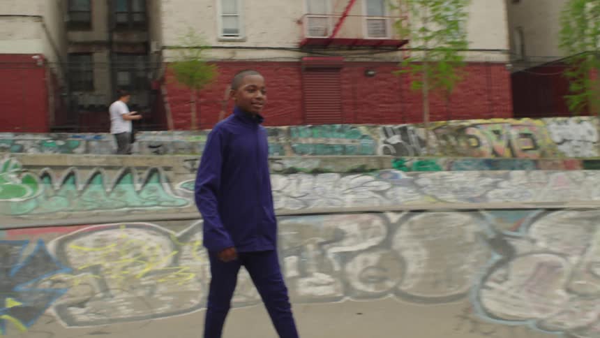 A young boy confidently practices soccer in a graffiti-filled urban skatepark in slow motion