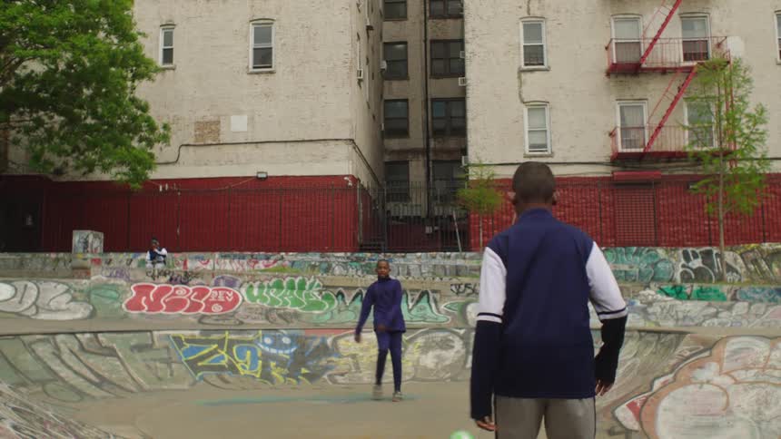 Two young men in matching tracksuits play with a soccer ball in a graffiti-covered urban skate park in slow motion