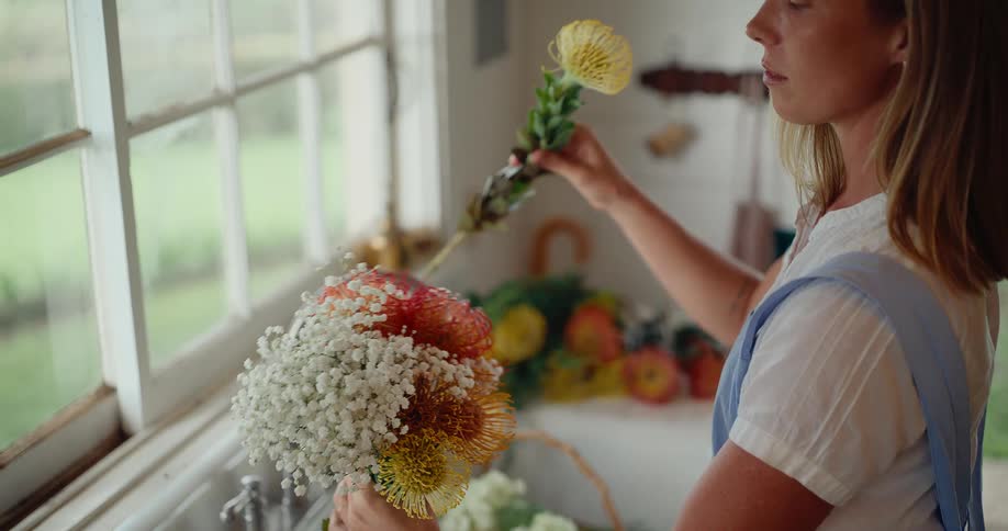 A woman in an apron carefully arranges a beautiful and colorful bouquet of fresh flowers in a rustic kitchen