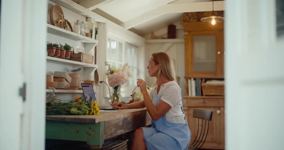 A slow tilt down through a doorway reveals a woman working on a laptop in her charming, rustic home studio
