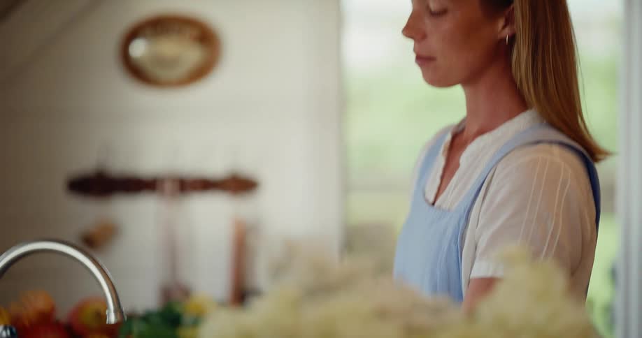 A woman in a rustic farmhouse kitchen gently rinses and prepares a bouquet of freshly cut flowers