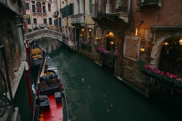 A serene view of a narrow canal in Venice, Italy, with moored gondolas gently bobbing on the water next to historic buildings