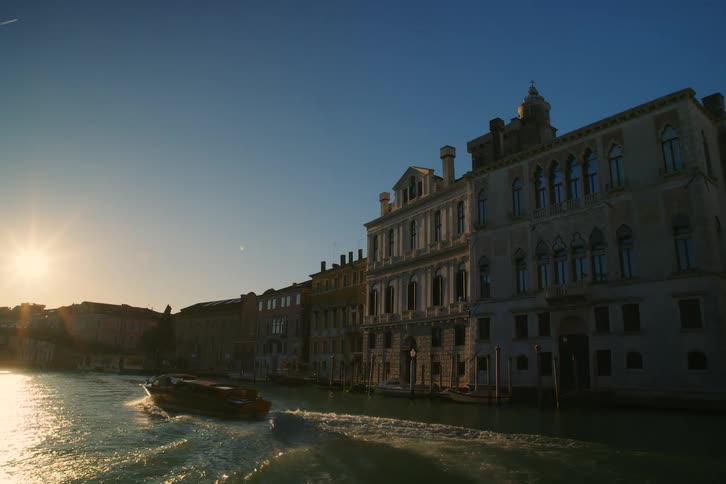 A water taxi travels down a sun-kissed canal in Venice, Italy, past stunning historic architecture at golden hour