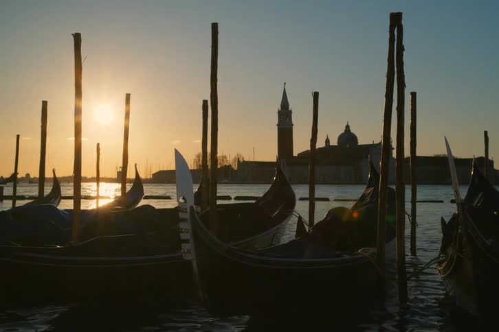 Silhouetted gondolas gently bobbing in the Venetian lagoon at sunrise with the Church of San Giorgio Maggiore in the background