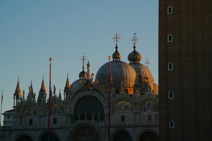 A close-up view of the ornate domes of Saint Mark's Basilica in Venice, Italy, glowing in the warm light of sunrise