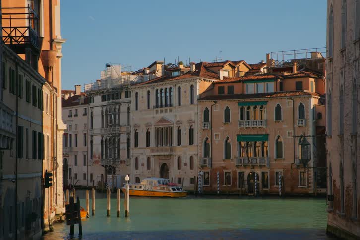 A bright yellow water taxi is moored in a sunlit canal, framed by historic Venetian buildings under a clear blue sky