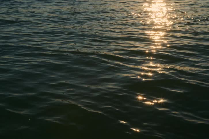 Golden sunlight glitters and sparkles on the surface of calm ocean waves