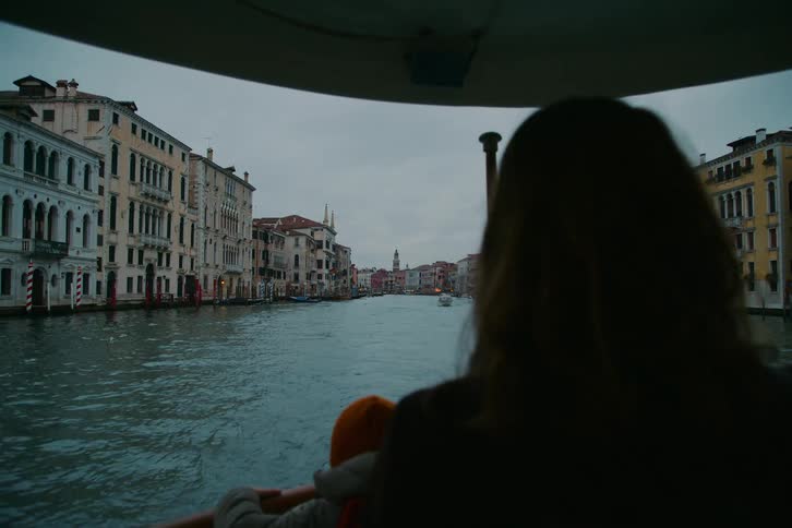 A mother and child in silhouette enjoy a boat ride along the Grand Canal in Venice on a cloudy evening