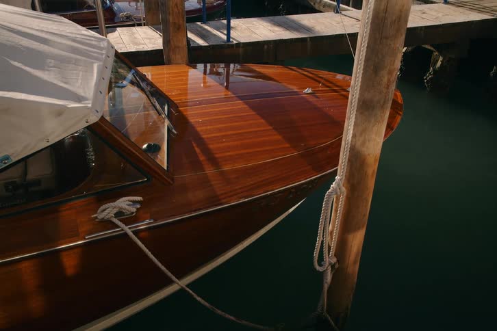 Sunlight gleams off the polished wood of a classic Italian motorboat moored in the tranquil waters of a canal