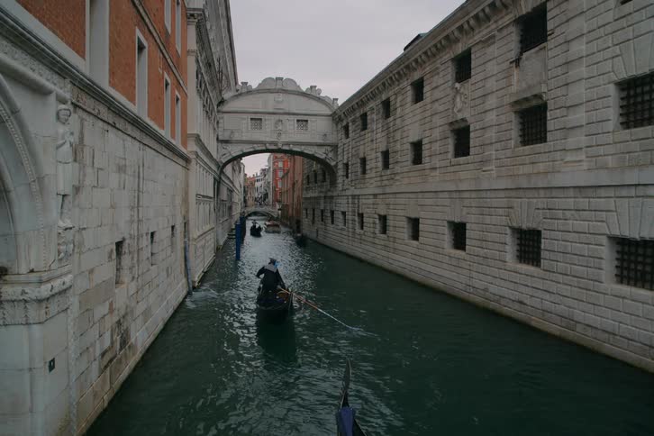 A gondolier paddles a boat with passengers through a narrow canal towards the famous Bridge of Sighs in Venice, Italy