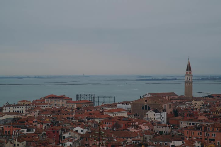 An aerial view of the historic red-roofed cityscape of Venice, Italy, overlooking the lagoon on a cloudy day