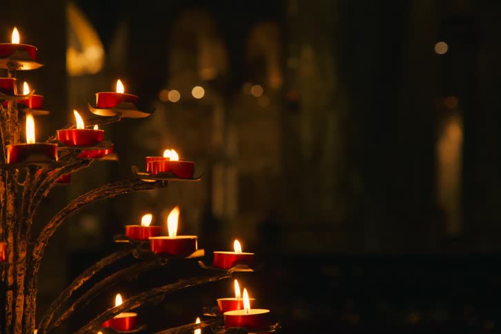 A close-up of numerous red tea light candles burning brightly in a candelabra inside a dark church