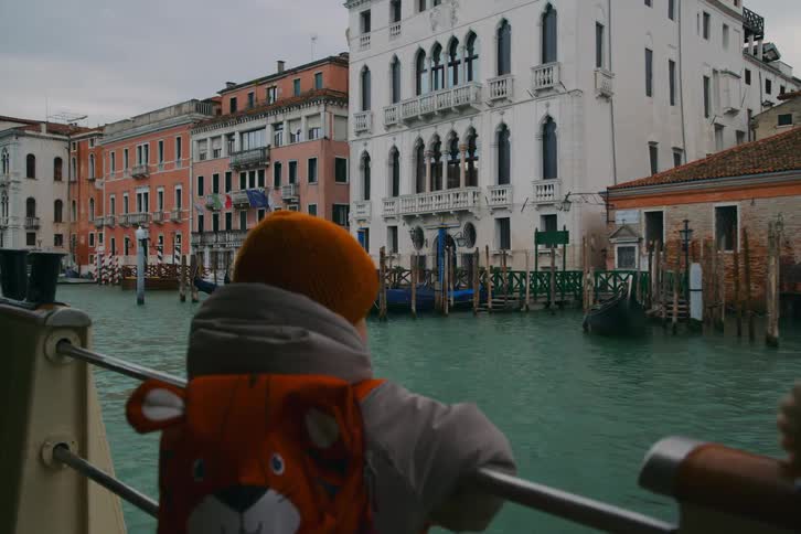 A young child with a tiger backpack enjoys a boat ride along the scenic canals of Venice, Italy