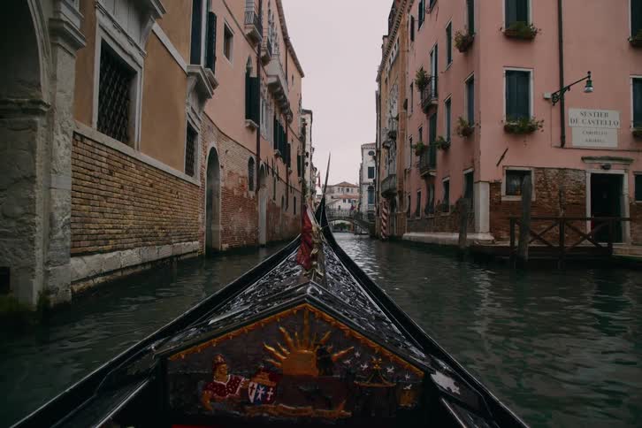 A first-person view from a traditional gondola gliding through a quiet, narrow canal in Venice, Italy