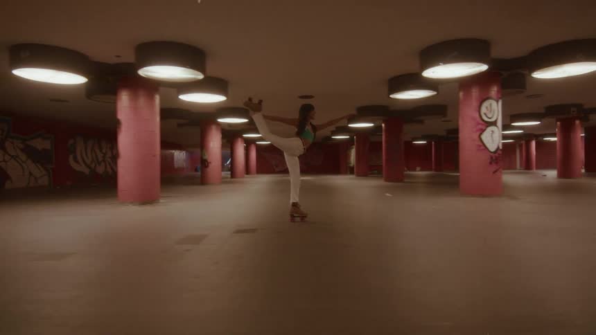 An artistic roller skater holds a graceful ballet pose while gliding through a moody, empty underground tunnel with pink pillars