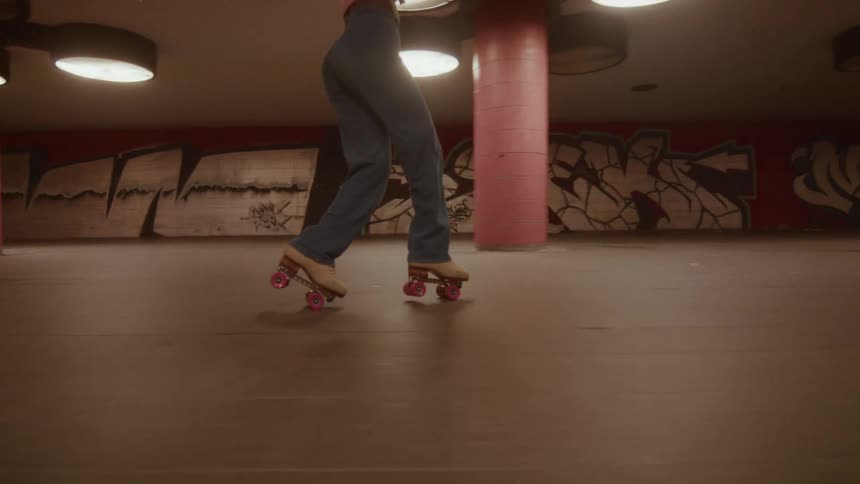 Low angle slow motion of a person's legs in flared jeans as they roller skate backwards through a graffiti-covered urban underpass