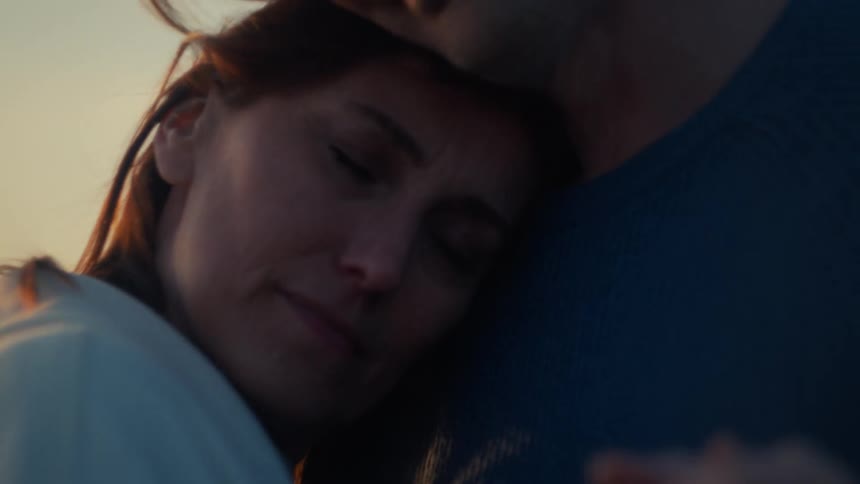 A serene woman rests her head on her partner's chest in a loving, intimate embrace during the golden hour