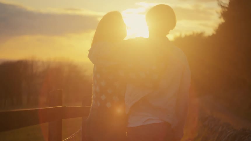 A romantic couple embraces and enjoys the golden hour sunset from a tranquil countryside path