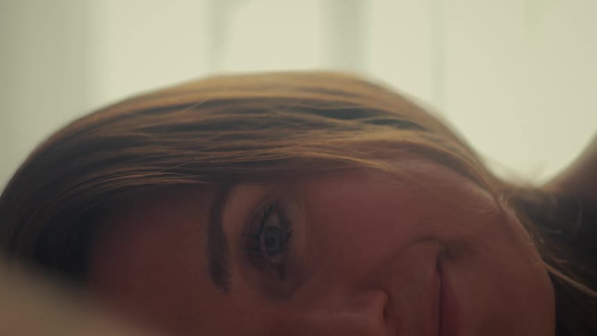 A serene woman with beautiful blue eyes smiles contentedly as she rests her head on a pillow